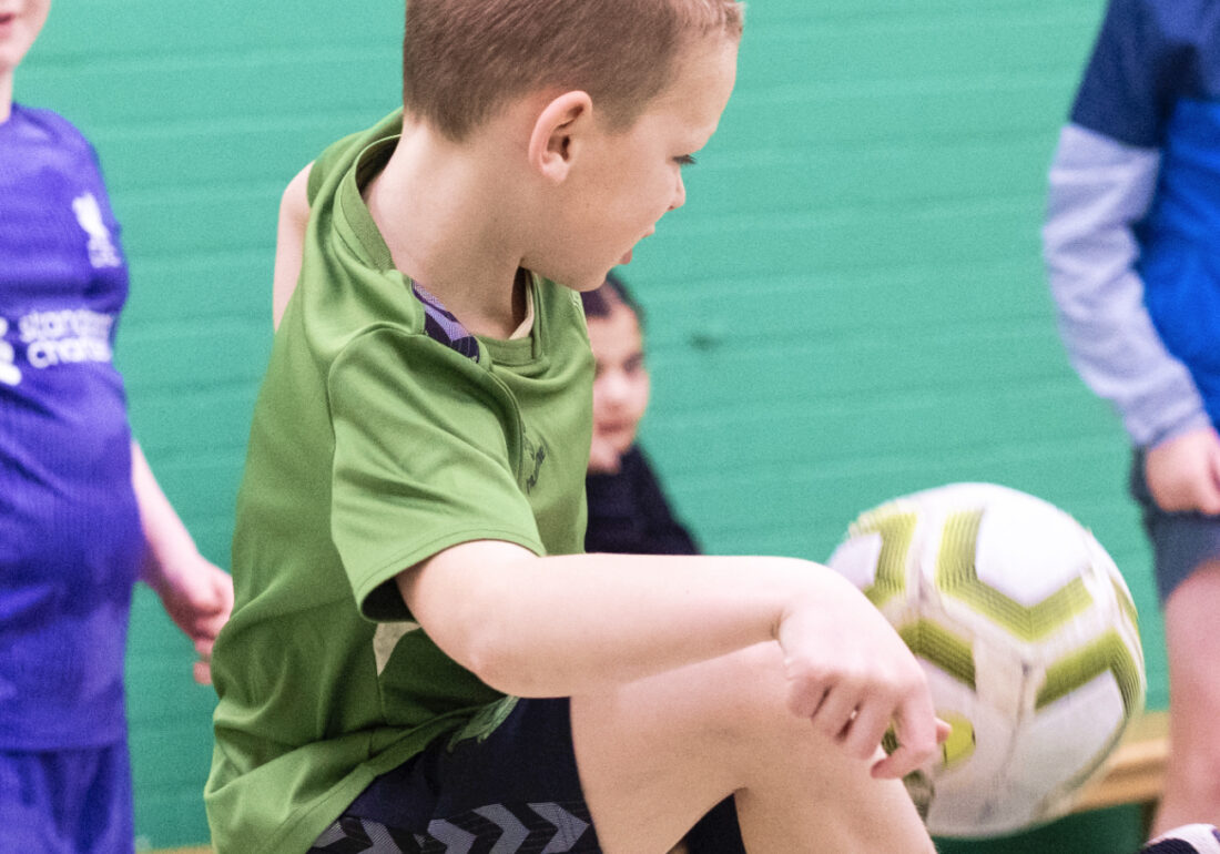 A young member of The Bronte youth club playing football in the sports hall at The Bronte Youth and Community Centre based in Liverpool City Centre