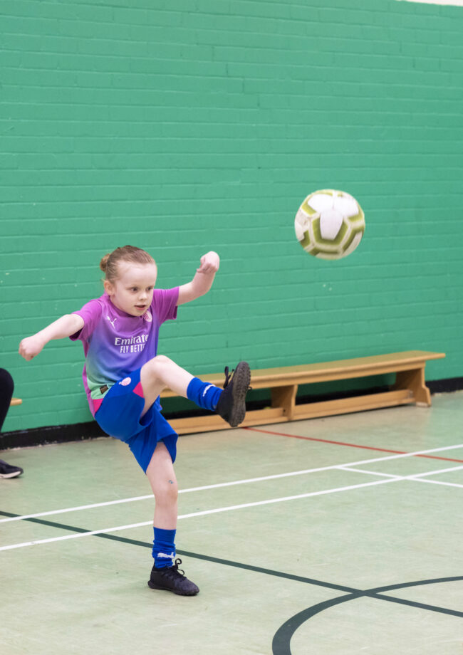 A young member of The Bronte youth club playing football in the sports hall at The Bronte Youth and Community Centre based in Liverpool City Centre