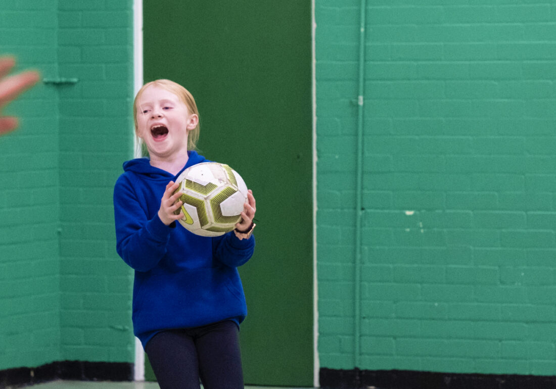A young member of The Bronte youth club playing football in the sports hall at The Bronte Youth and Community Centre based in Liverpool City Centre