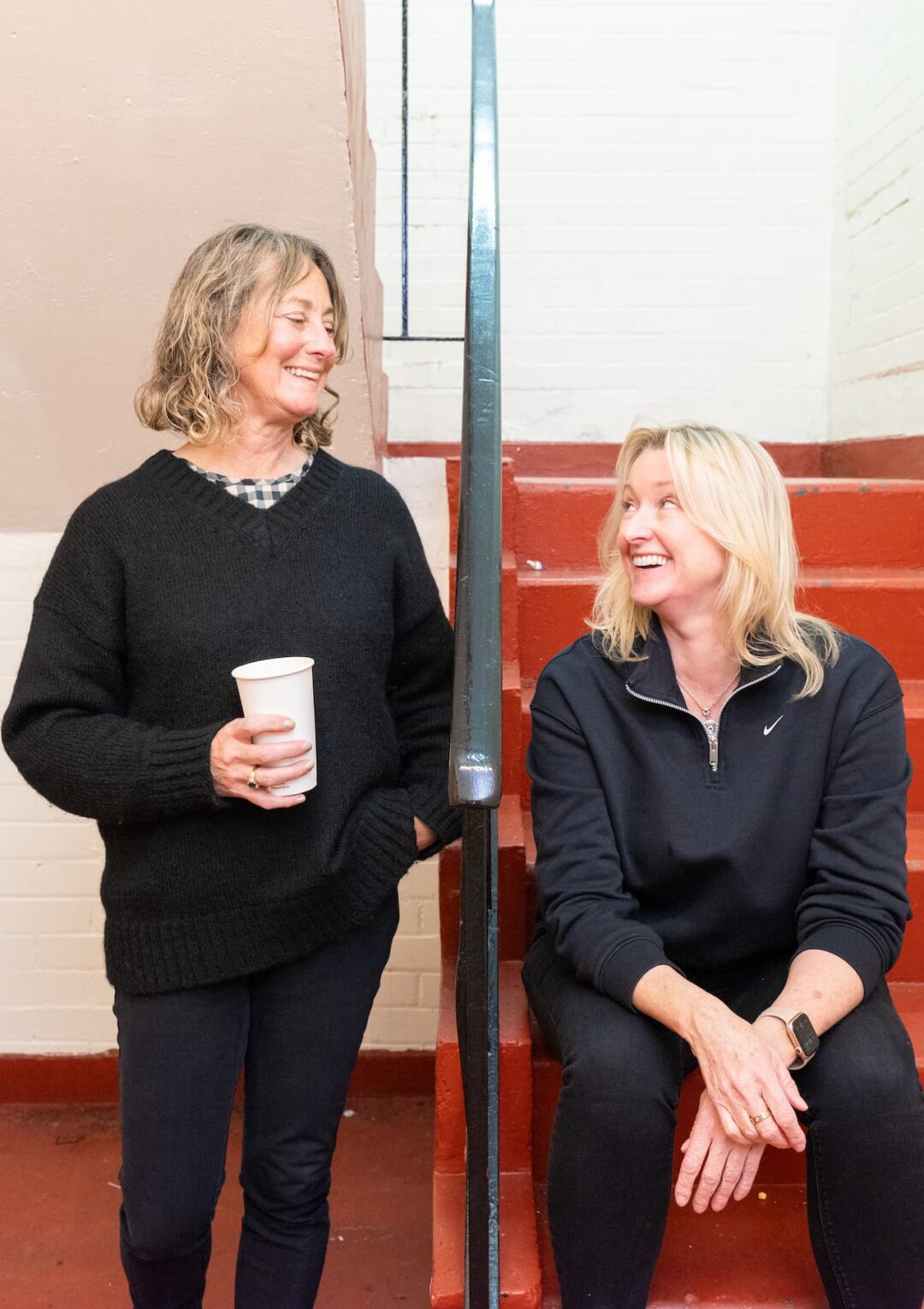 Two members of The Bronte staff smiling, one sat on the stairs of the building based in Liverpool City Centre